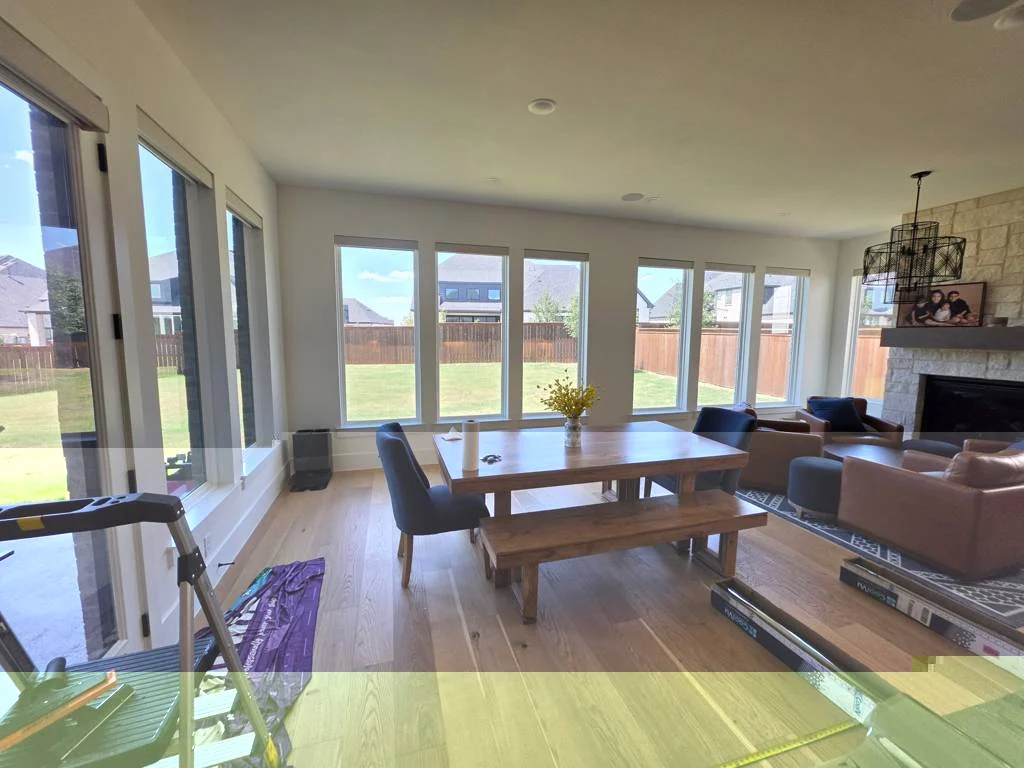 Sunlight through the windows of a dining and living room during a window-tint installation, with installation tools visible.